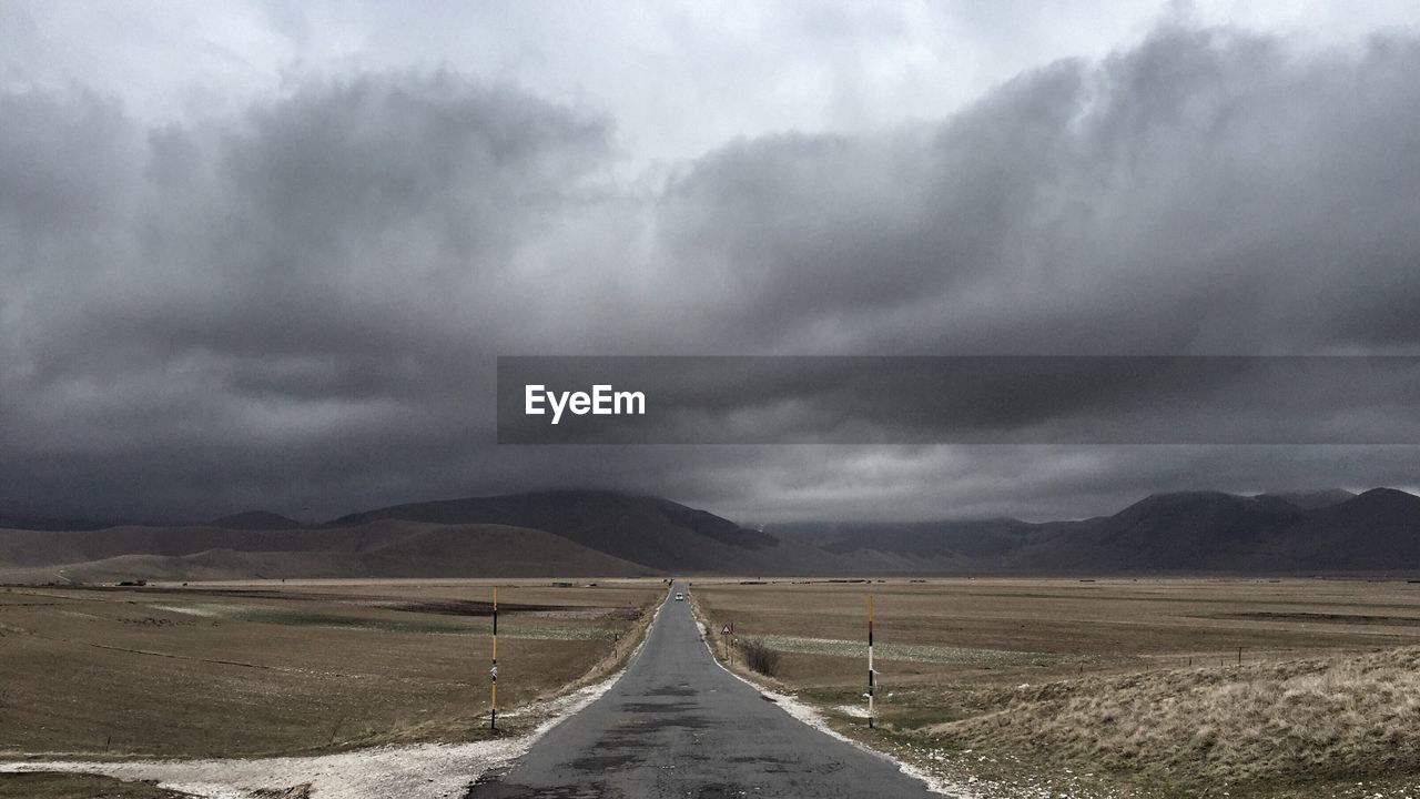 Road leading towards mountains against cloudy sky