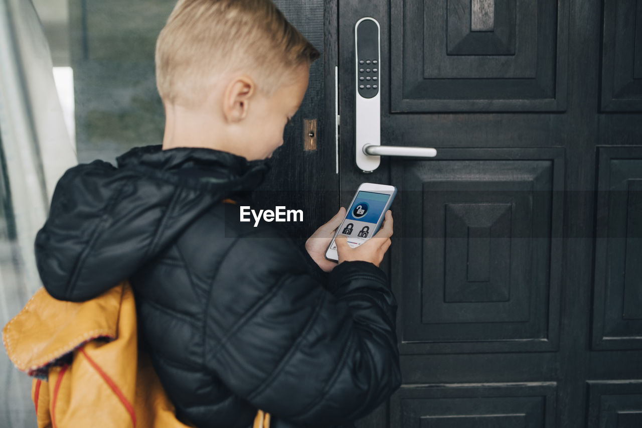 Rear view of boy using app on smart phone to unlock house door