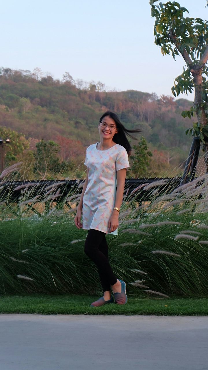 Portrait of young woman standing on grassy field against hill