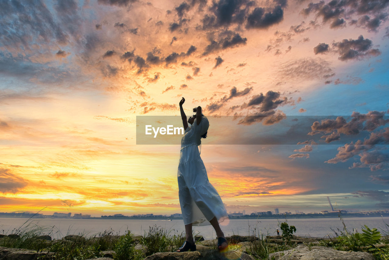 Woman standing by sea against sky during sunset