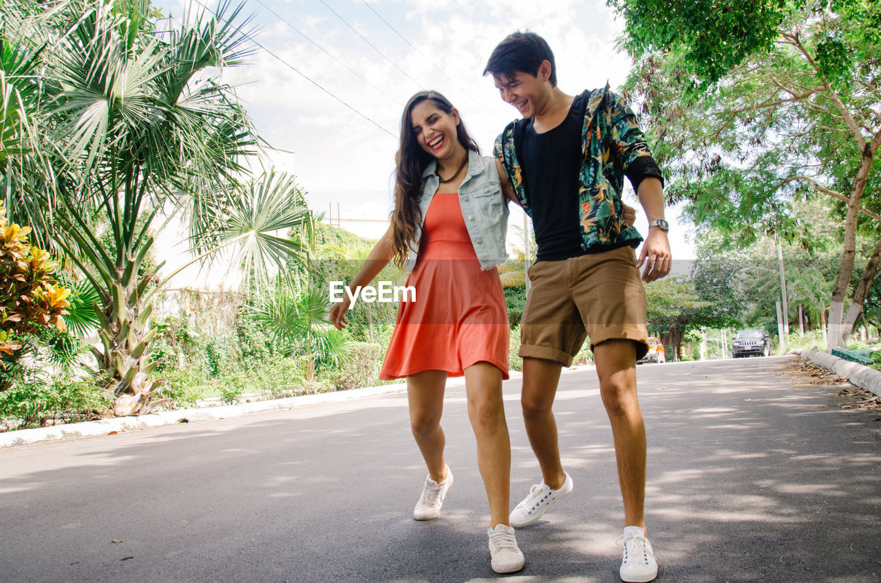 Full length of happy playful friends walking on road against sky