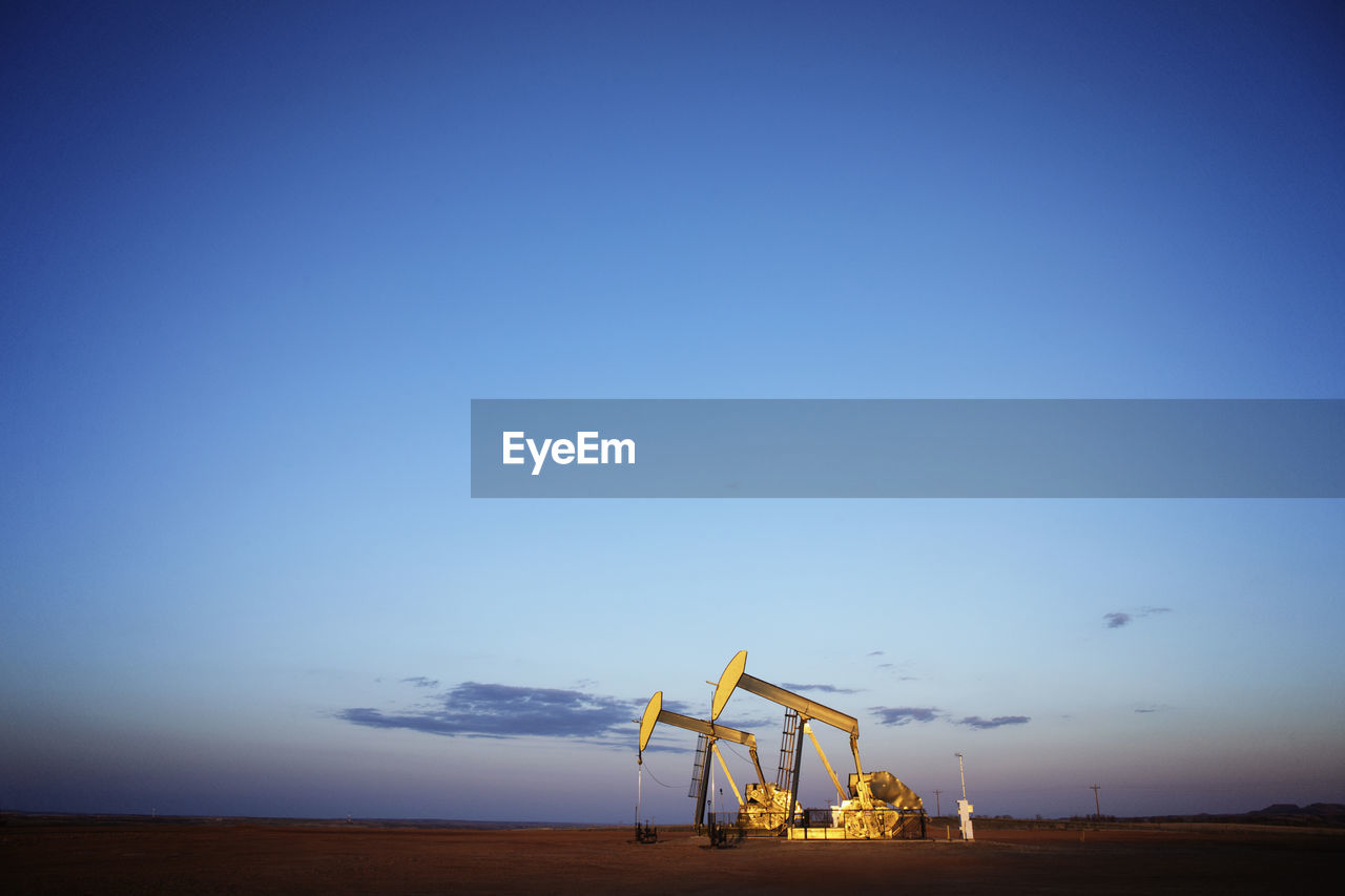 Oil pumps on field against blue sky