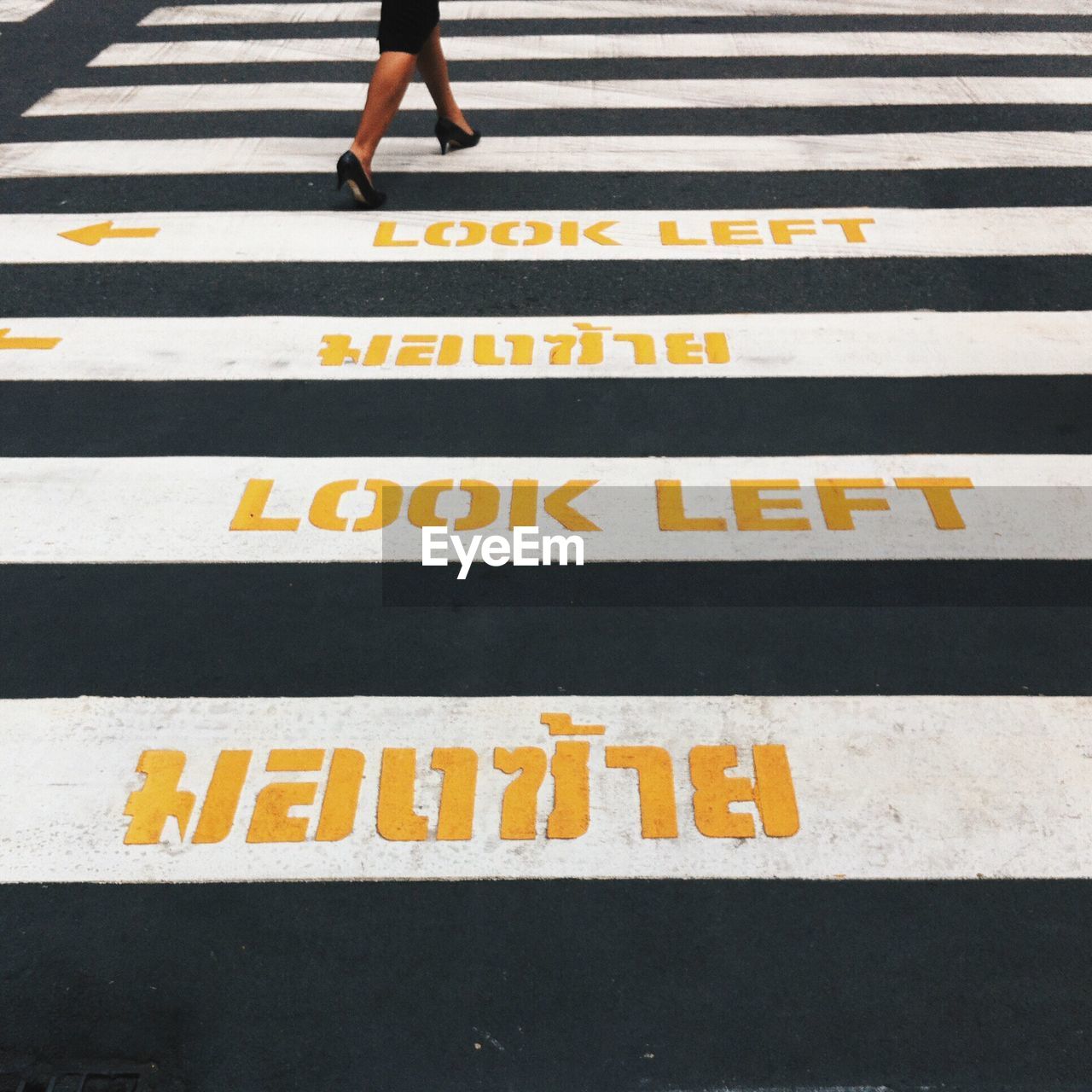 Low section of woman walking on zebra crossing road sign