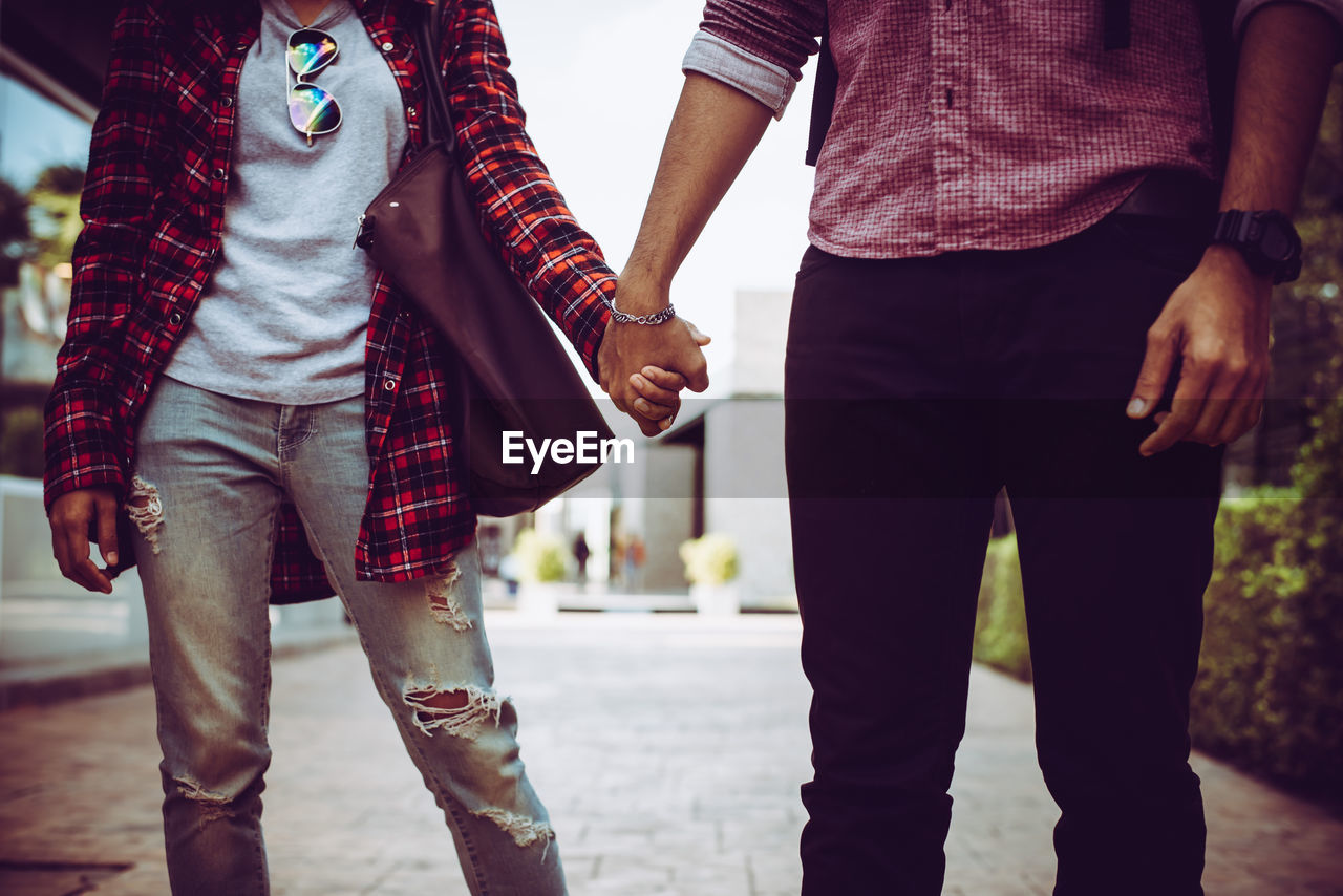 Midsection of couple holding hands on street in city