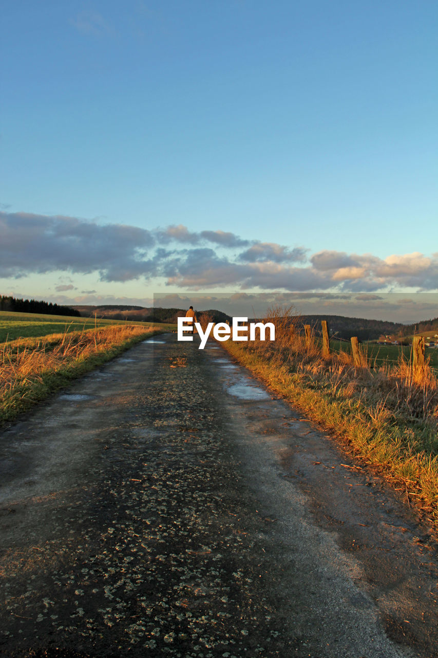 Road leading towards man amidst landscape at sunset