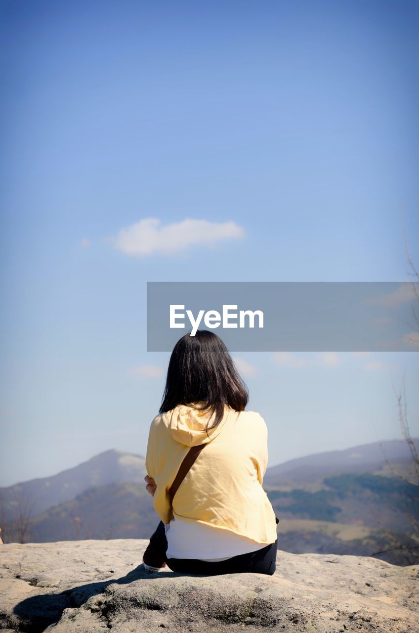 Rear view of girl sitting on mountain against blue sky