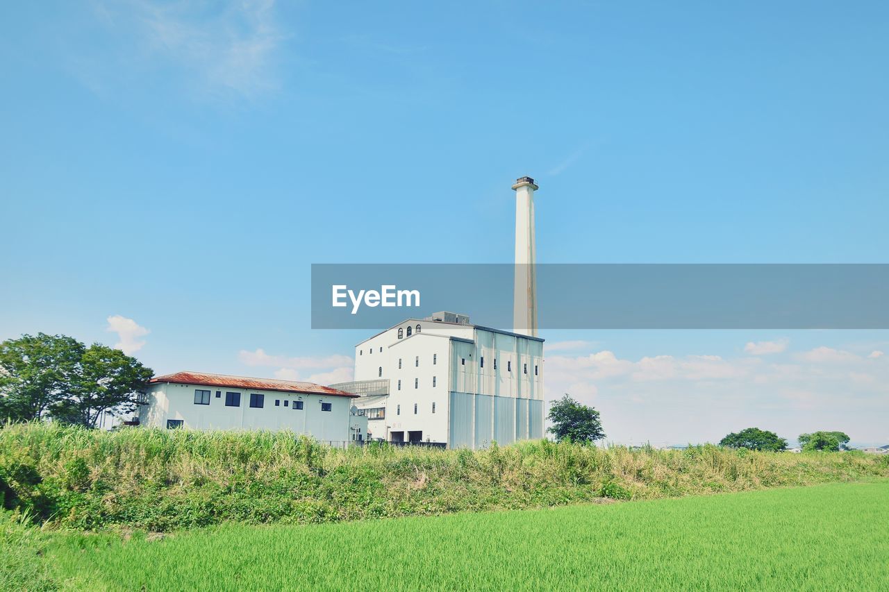 sky, architecture, built structure, plant, building exterior, field, nature, grass, rural area, land, landscape, environment, building, day, no people, green, agriculture, blue, rural scene, outdoors, prairie, cloud, tower, tree, plain, growth, wind, windmill, factory, copy space, farm, hill, horizon, environmental conservation, crop, industry, power generation