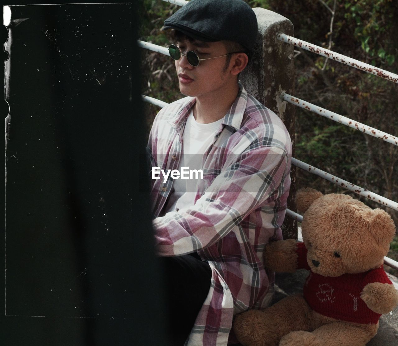 Thoughtful young man with teddy bear sitting on footbridge