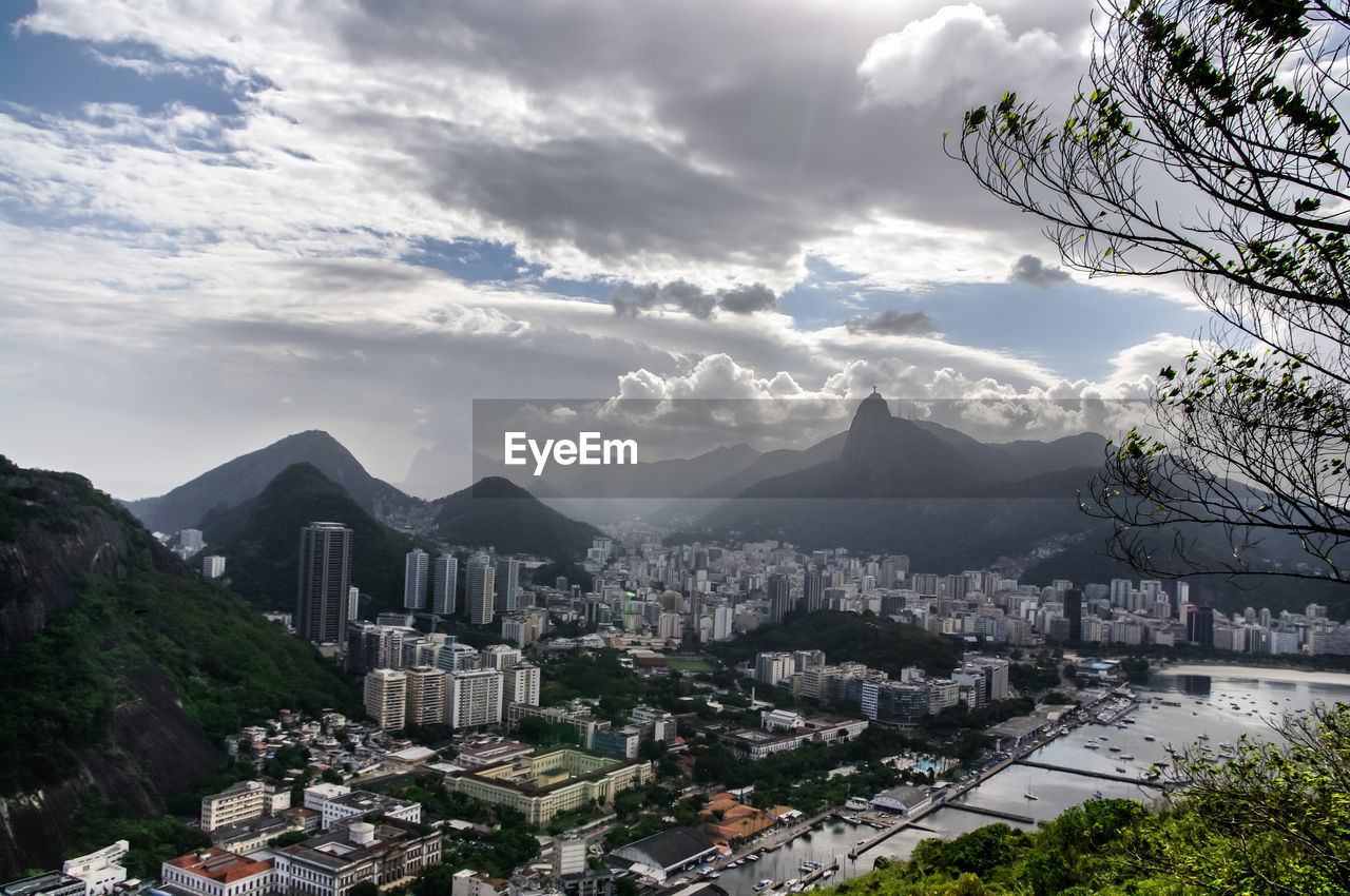 Aerial view of cityscape by mountains against cloudy sky