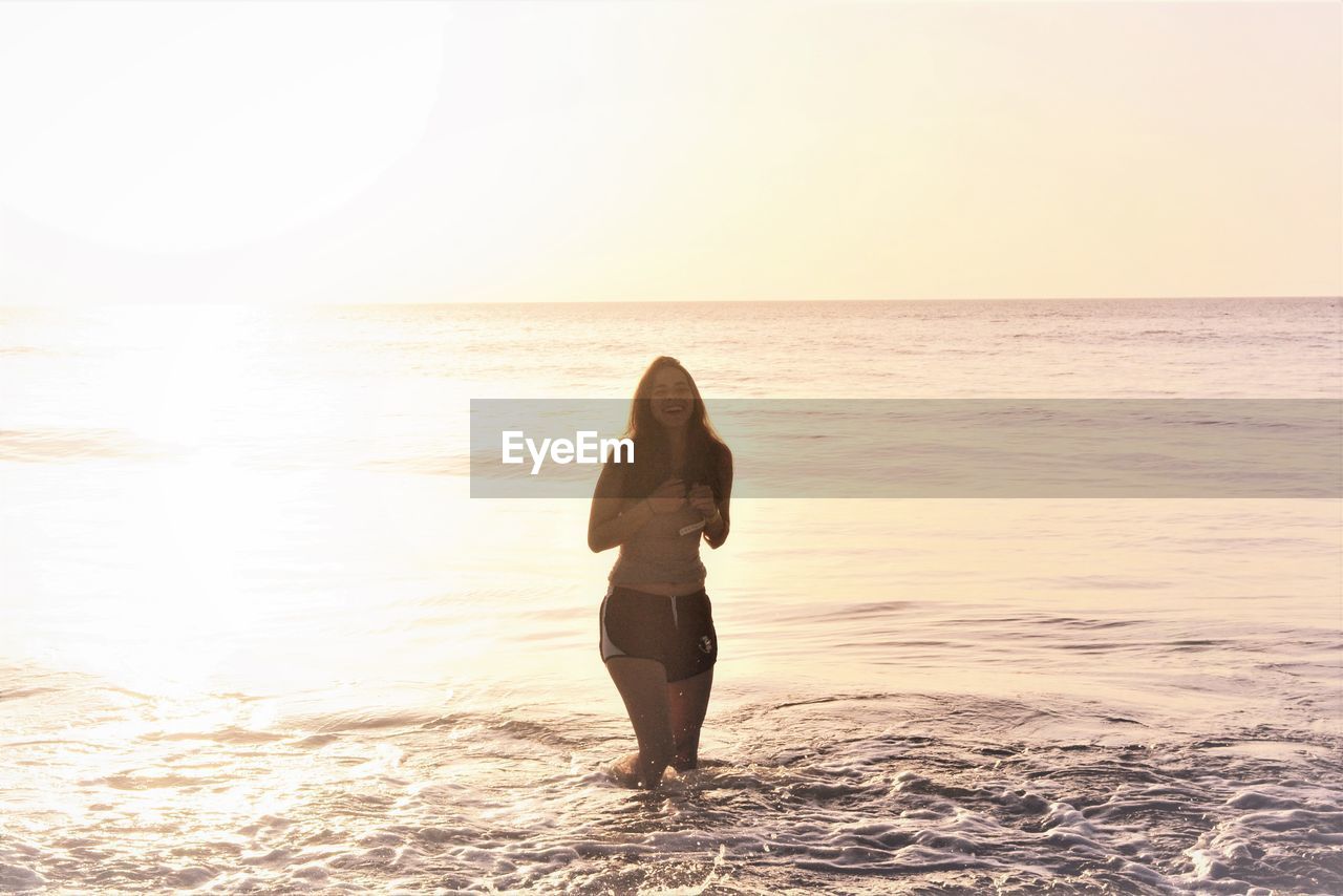 Happy young woman girl enjoying the ocean having fun at the beach under sky during sunrise or sunset