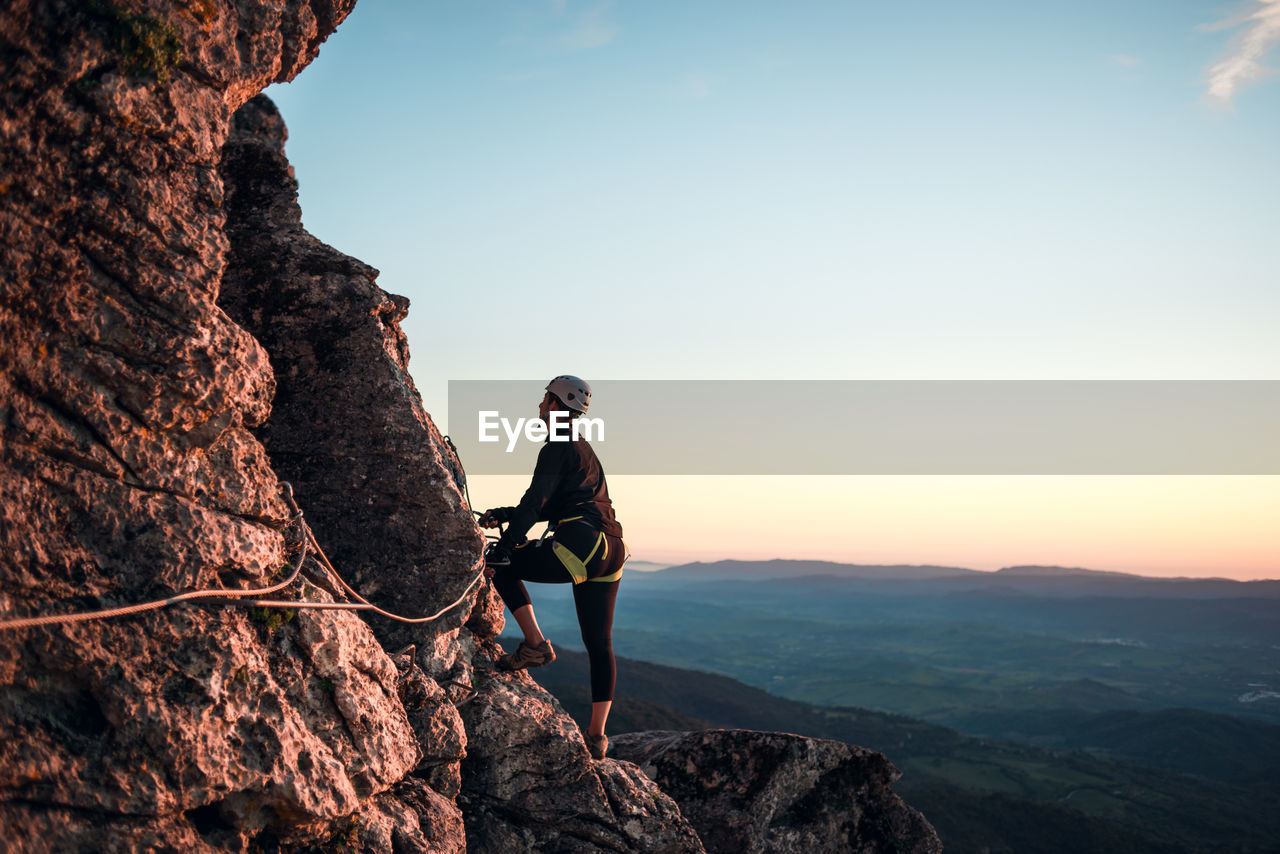 Concept: adventure. climber woman with helmet and harness. silhouette at sunset on the mountain. profile. resting looking at the climbing route. via ferrata in the mountains.