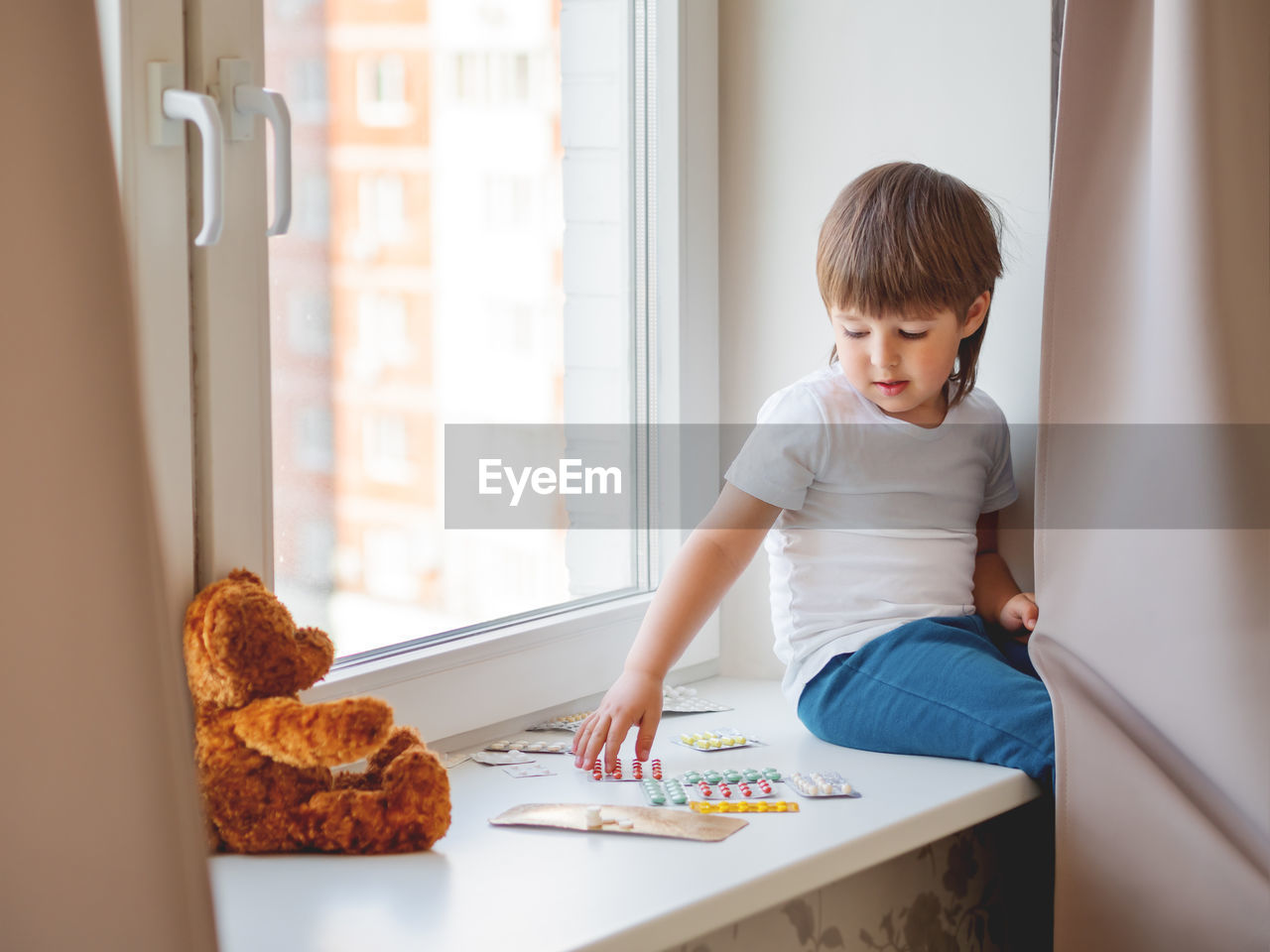 Toddler sits on windowsill and plays with scattering pills without parent's control. 