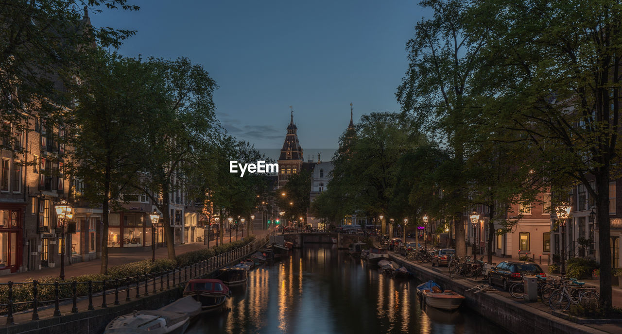 Illuminated rijksmuseum and canal in spiegelgracht against sky at night