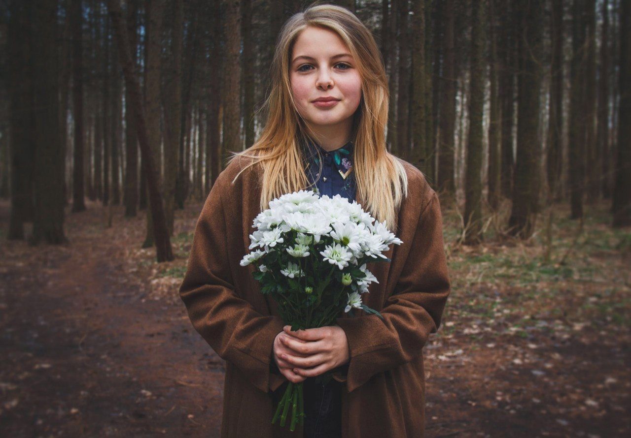 Portrait of a young woman holding bouquet against tree trunks