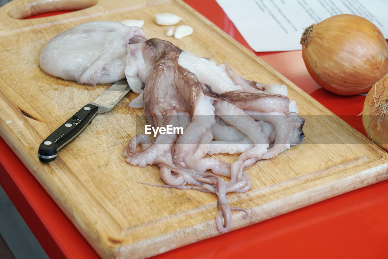 High angle view of dead octopus with knife on cutting board by onions