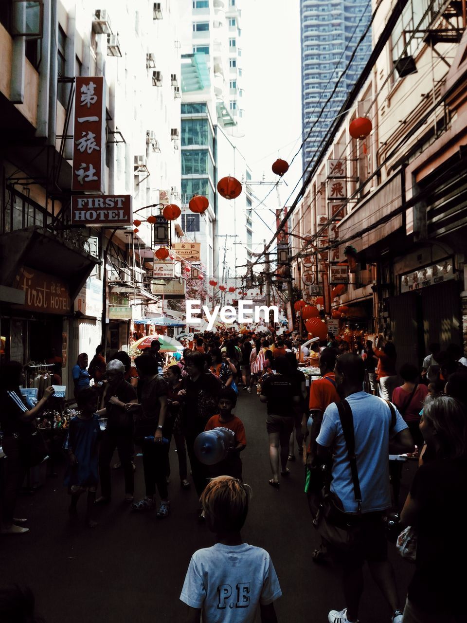 GROUP OF PEOPLE WALKING ON CITY STREET AMIDST BUILDINGS IN BACKGROUND