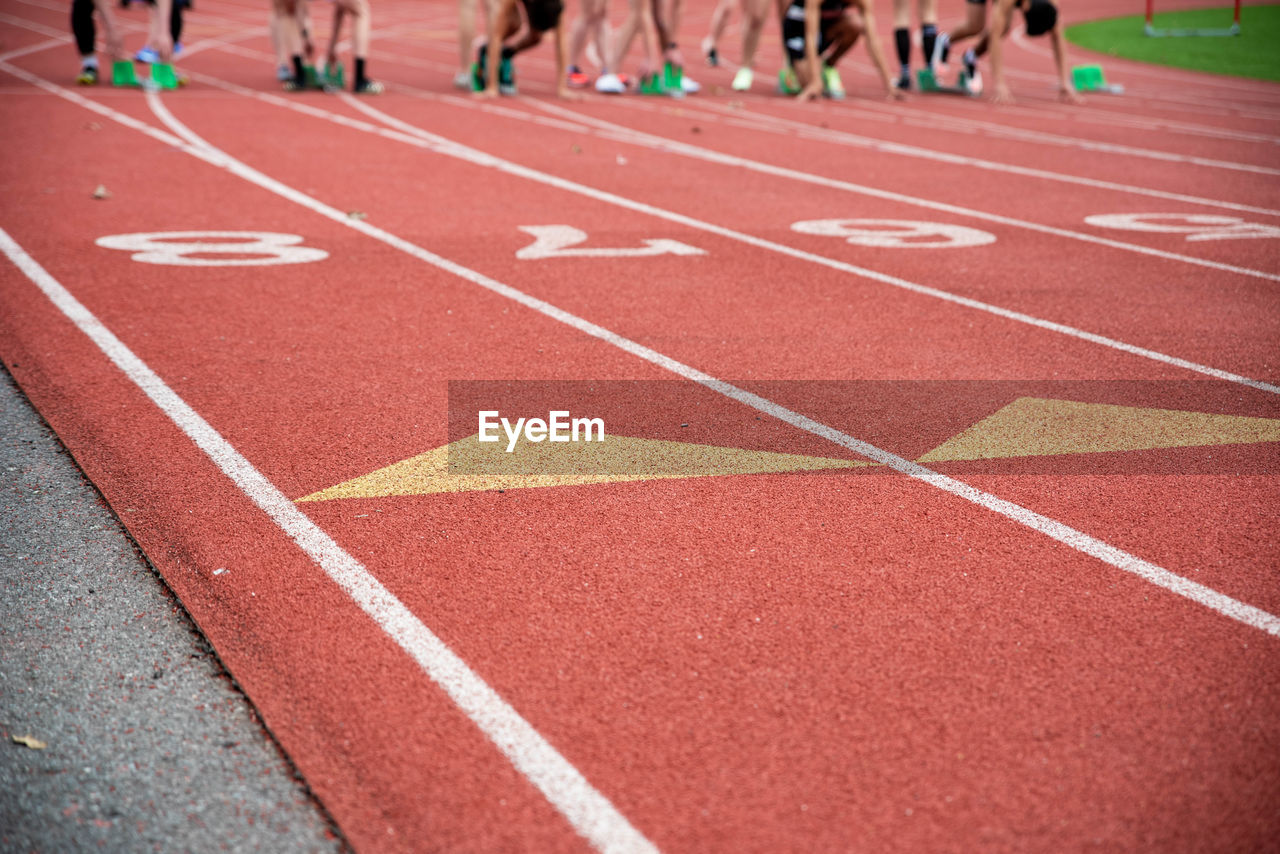 Runners at the starting line on blocks at an athletic racing track with numbers and lane markings