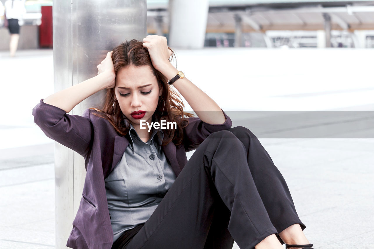 Tensed young businesswoman sitting on walkway 