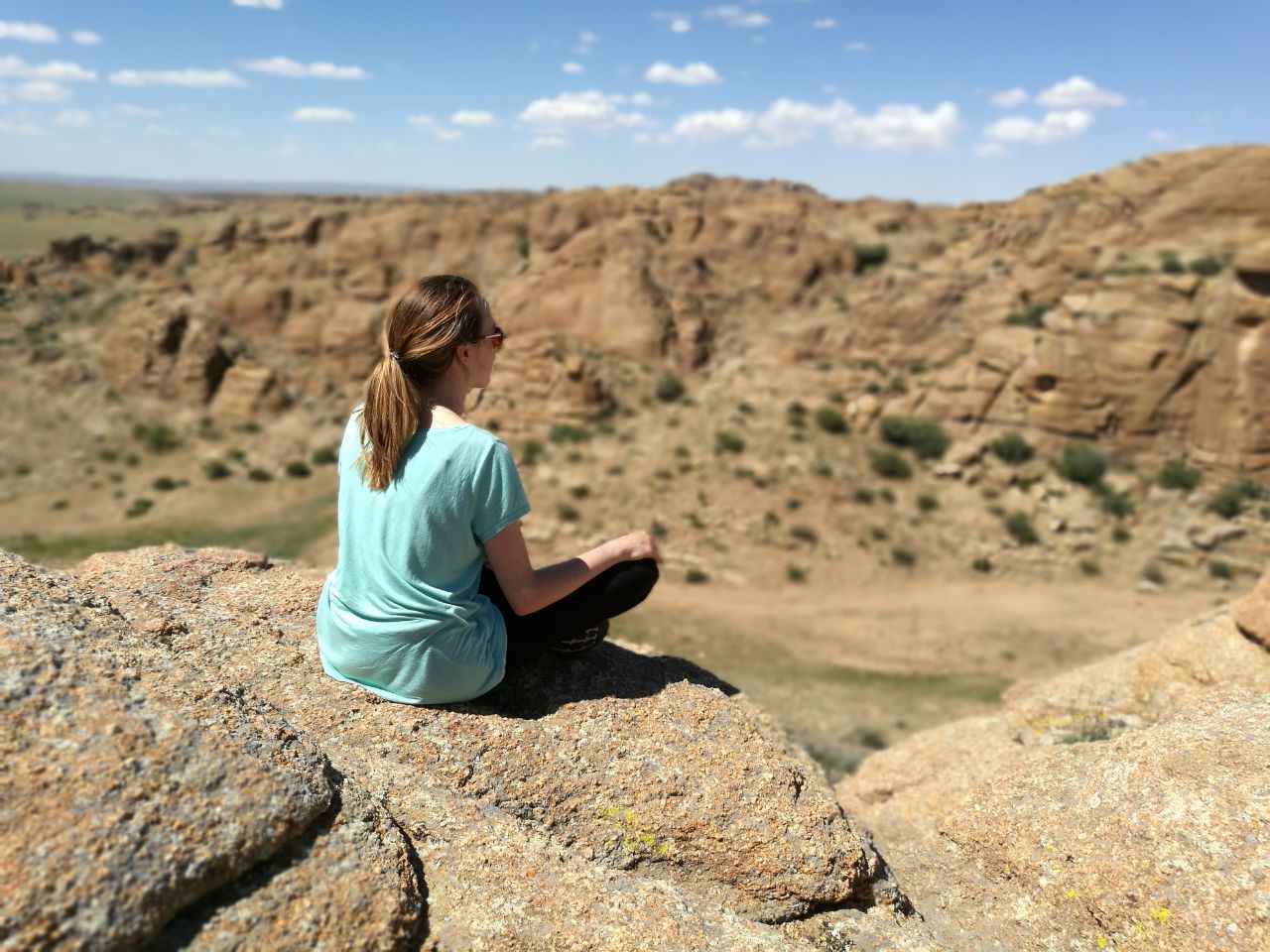 Woman sitting on rock at landscape against sky