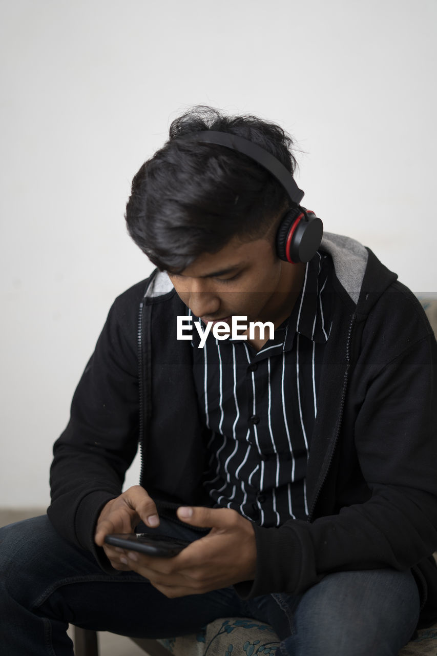 Indian teenager boy black jacket with headphone sitting on floor at home. handsome guy.