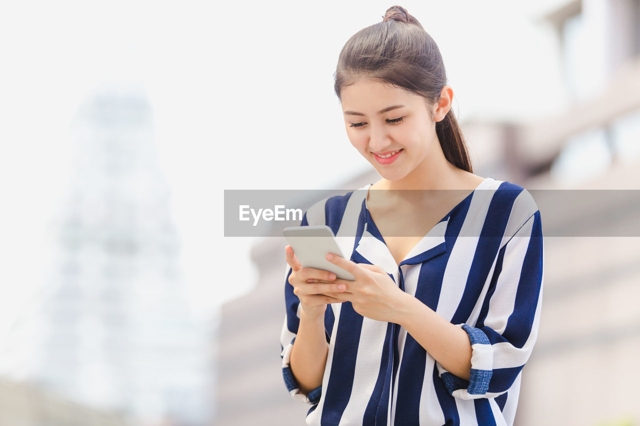 Smiling young woman using mobile phone while standing in city