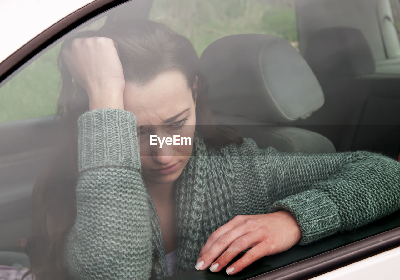 Tensed woman sitting in car seen through window