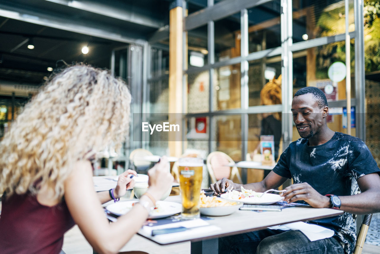 Blond woman and african man enjoy eating in restaurant.