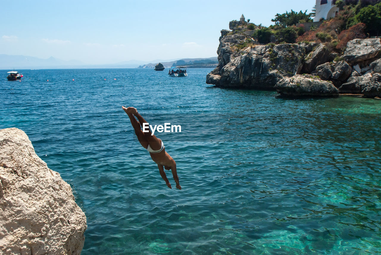 MAN JUMPING ON ROCK IN SEA