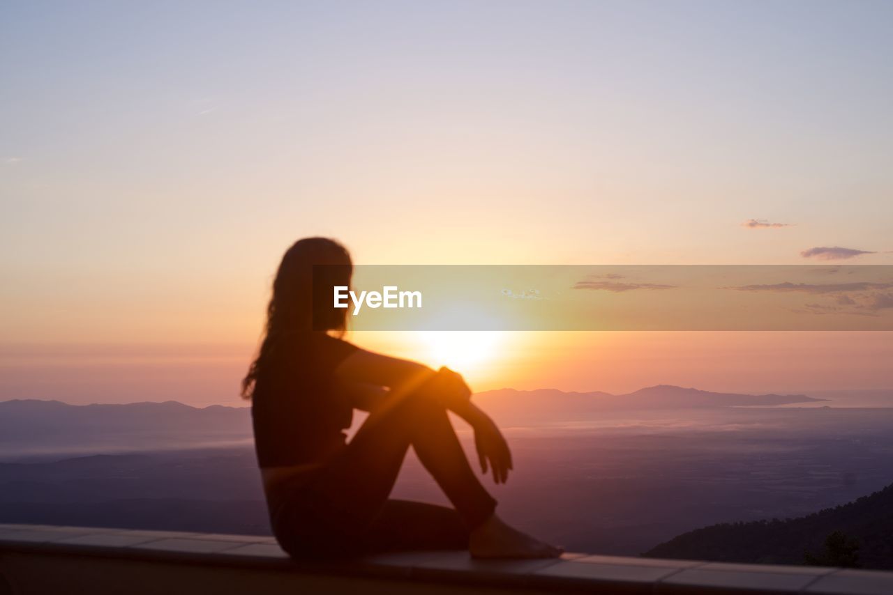 Silhouette man sitting on mountain against sky during sunset