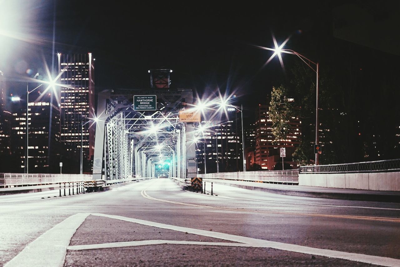 Illuminated bridge leading towards city against clear sky at night