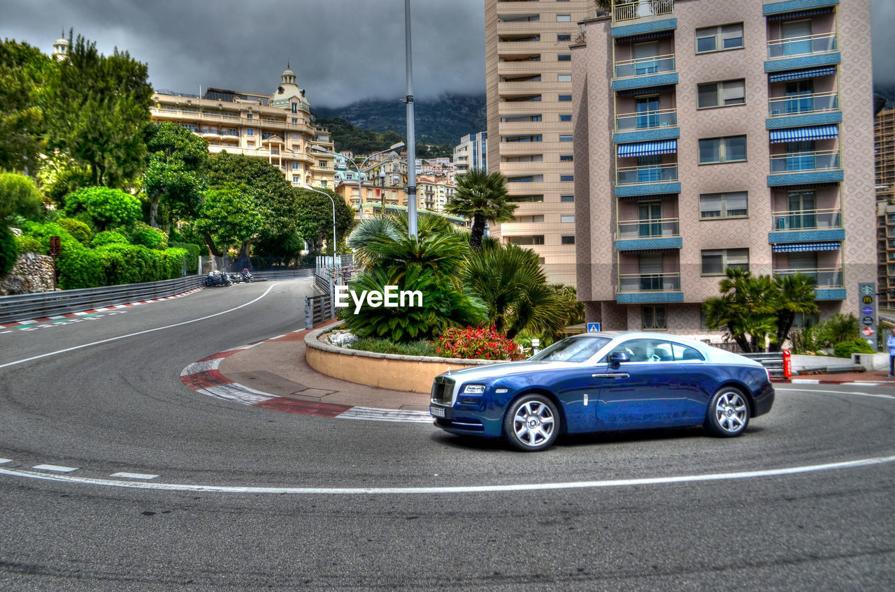 CAR ON ROAD BY BUILDINGS AGAINST SKY