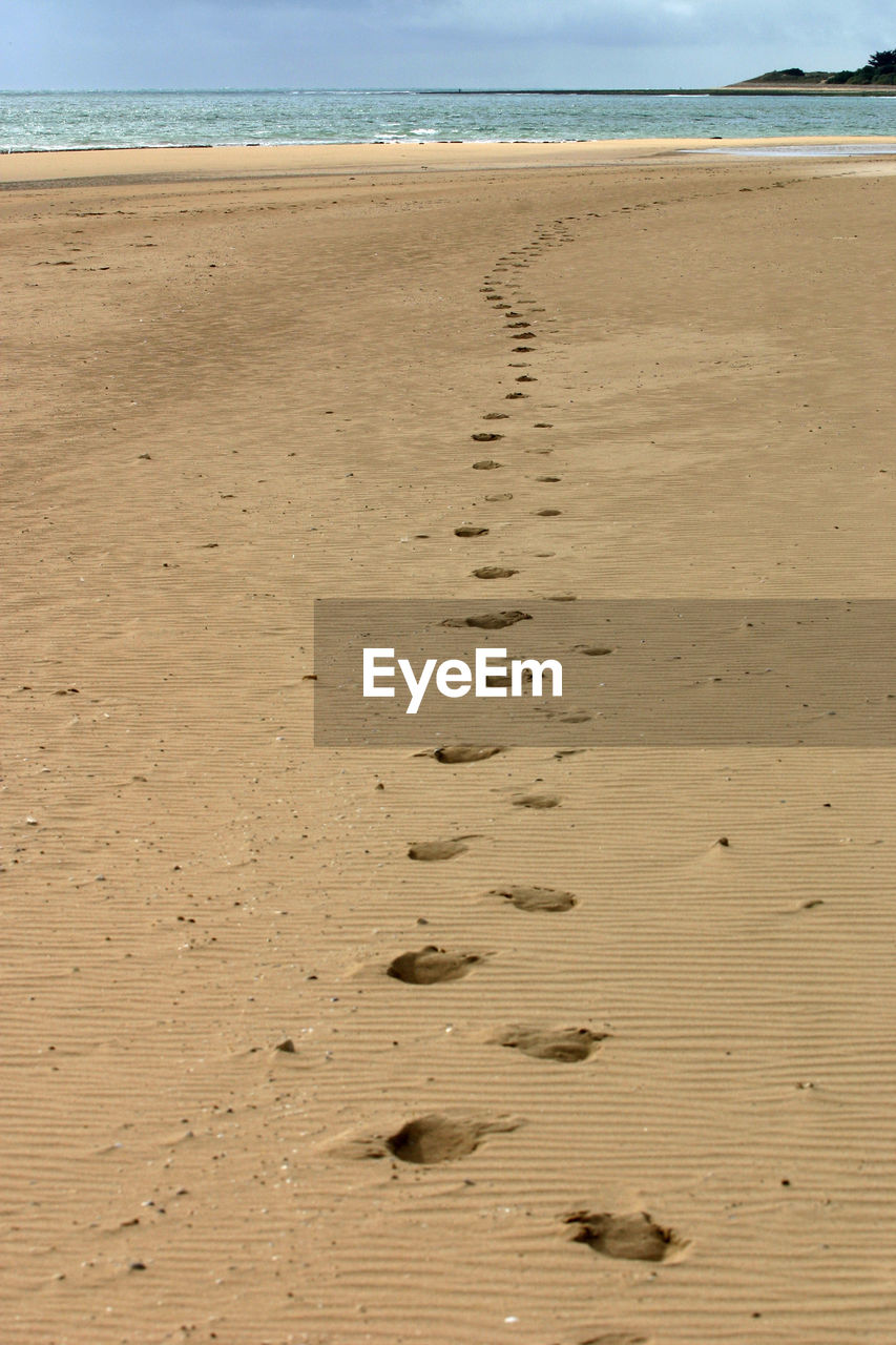 Footprints on sand at beach against sky