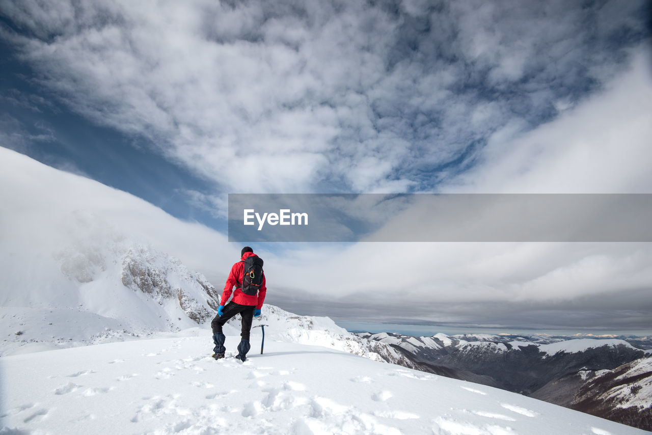 Rear view of man walking on snowcapped mountain against sky