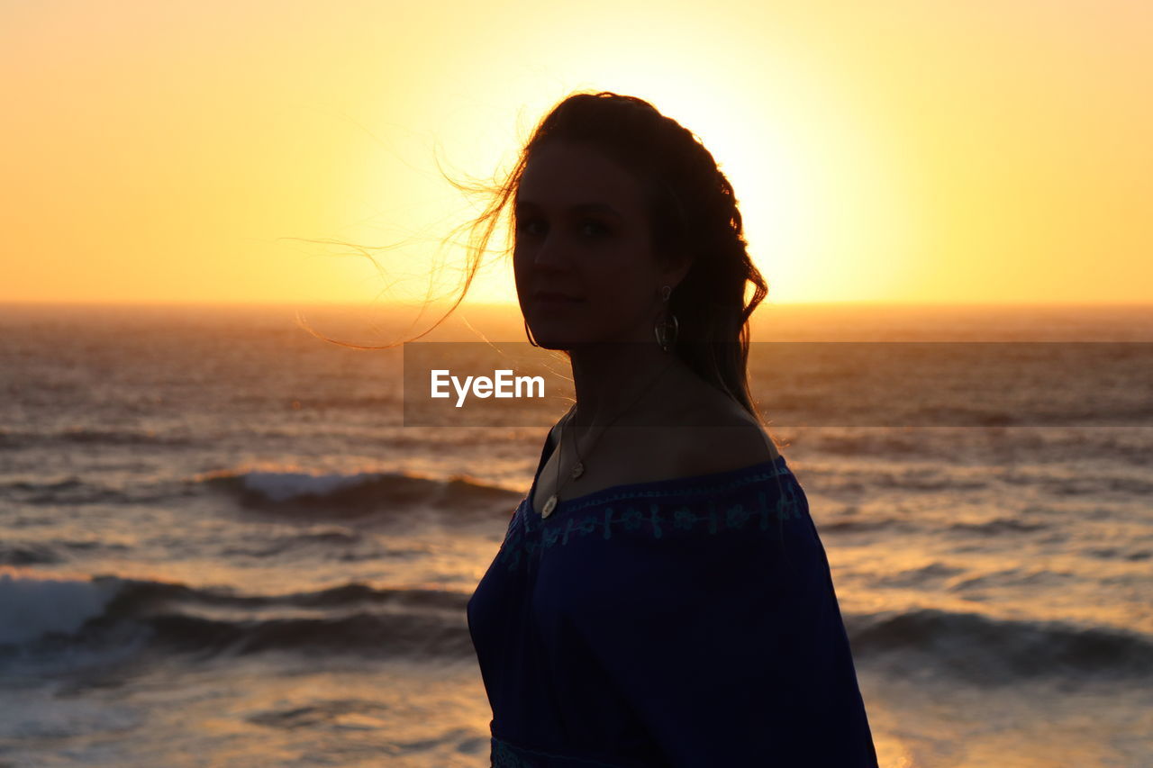 Woman standing at beach against sky during sunset