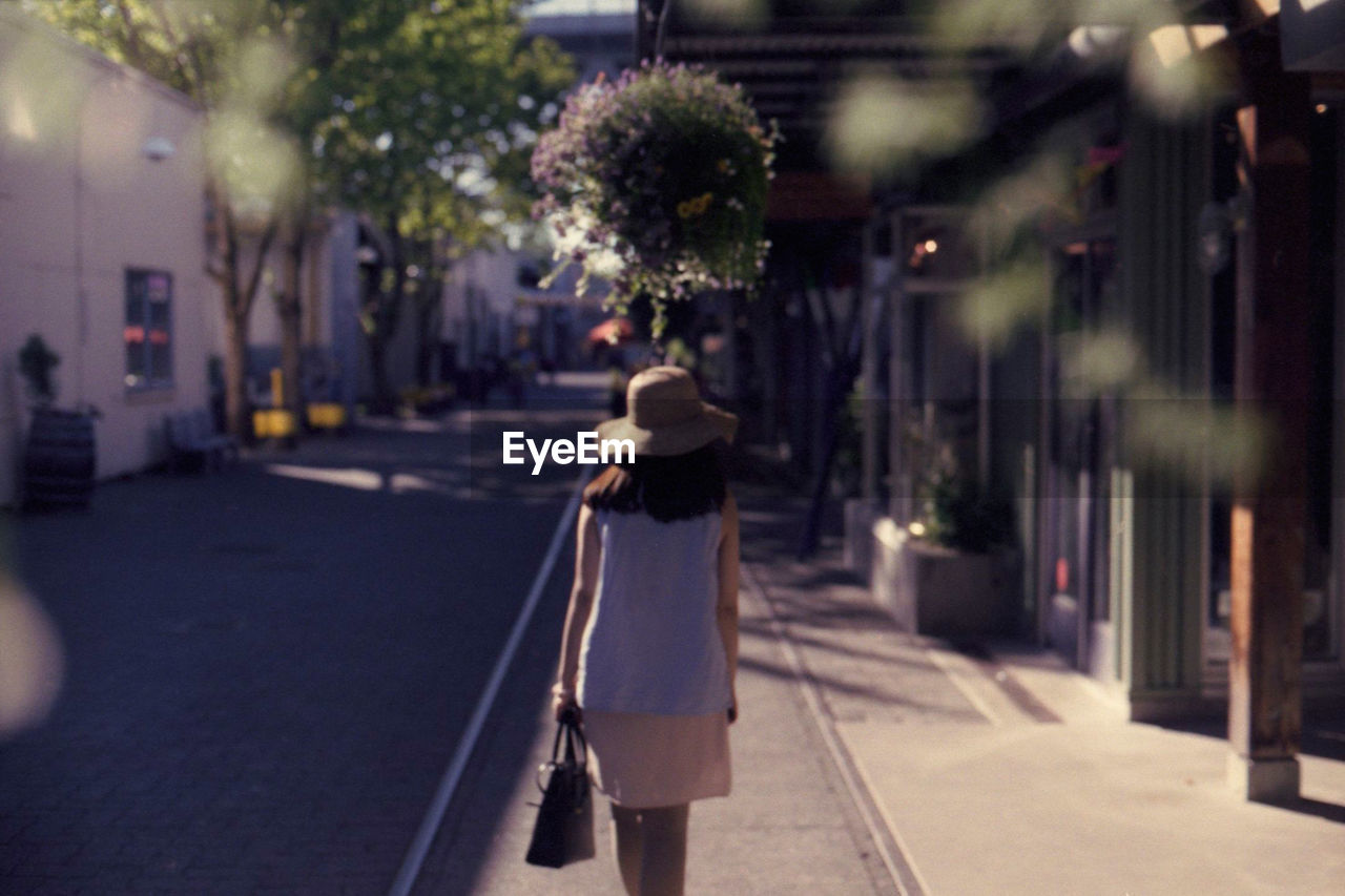Rear view of woman walking on sidewalk during sunny day