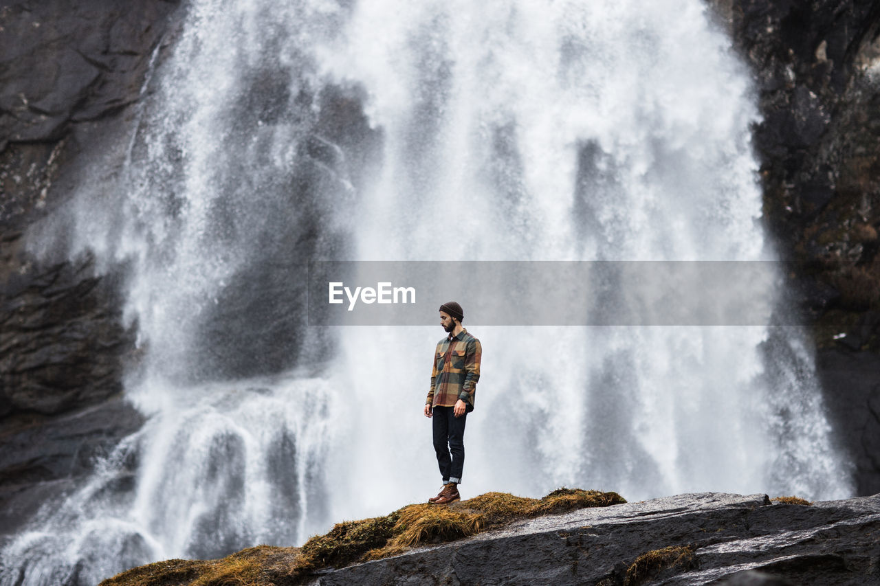 Male hiker standing on hill near waterfall in highland area in winter