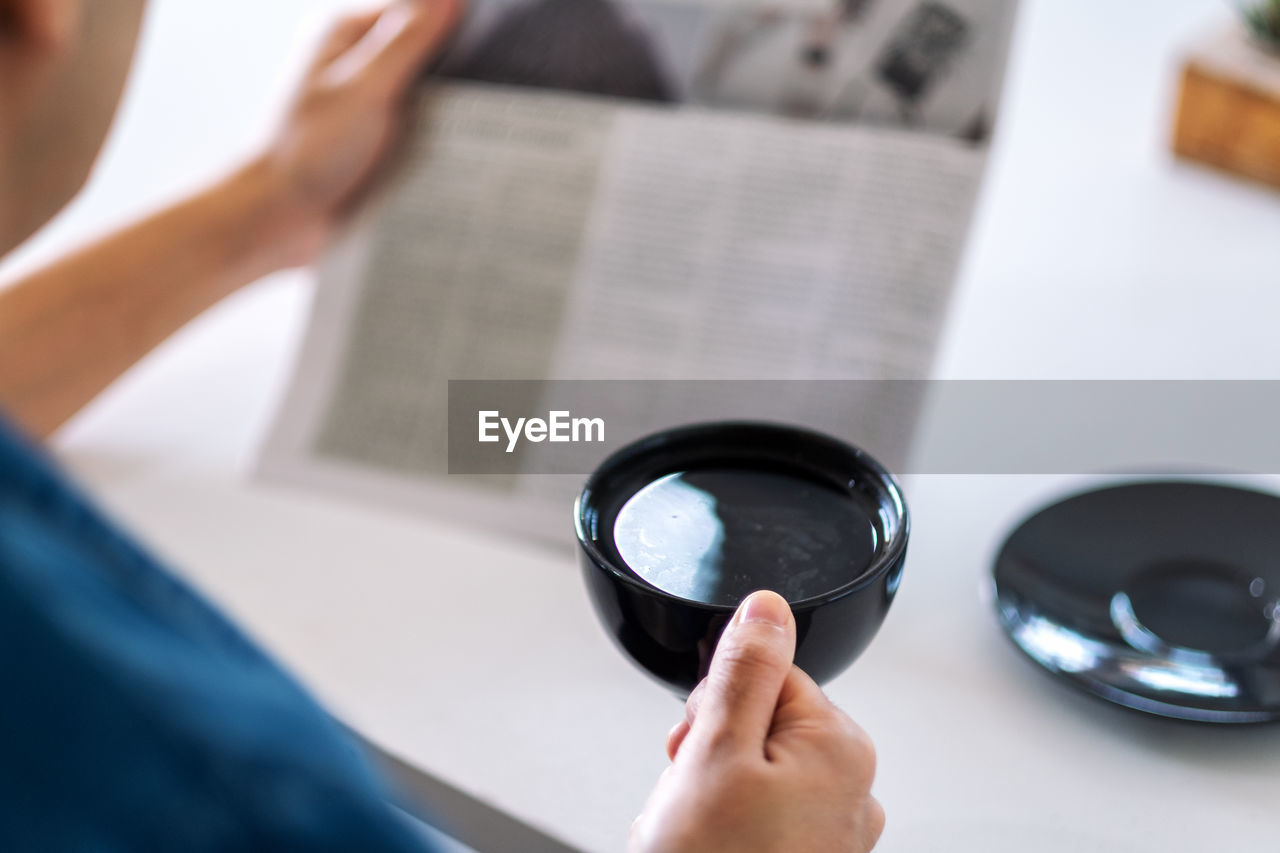 Cropped image of man having coffee while reading newspaper at table