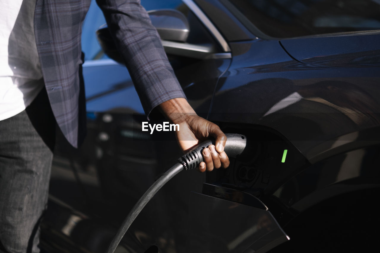 Hand of man plugging charger into electric car