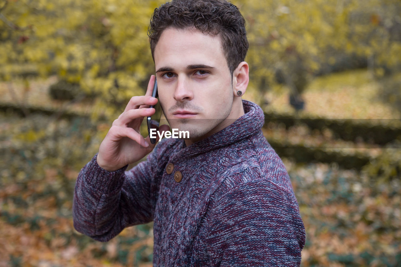 Portrait of young man talking on smart phone while standing in park during autumn