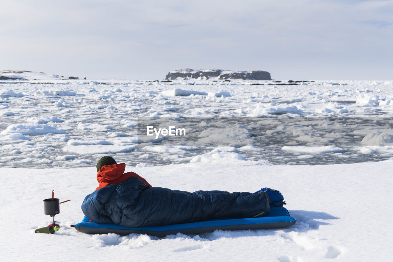 Male hiker resting in sleeping bag on snow covered land