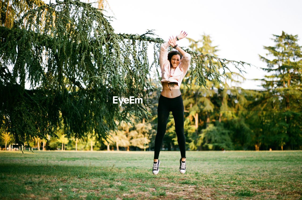 Cheerful young woman jumping over grassy field at park