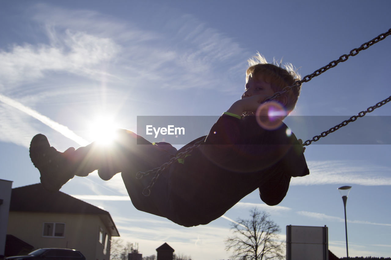 Low angle view of boy playing on swing during sunny day
