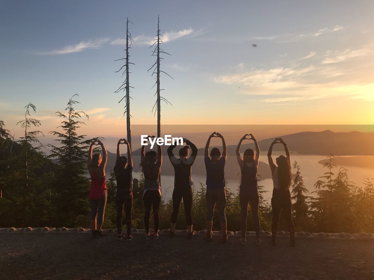 Rear view of people with arms raised making heart shape during sunset