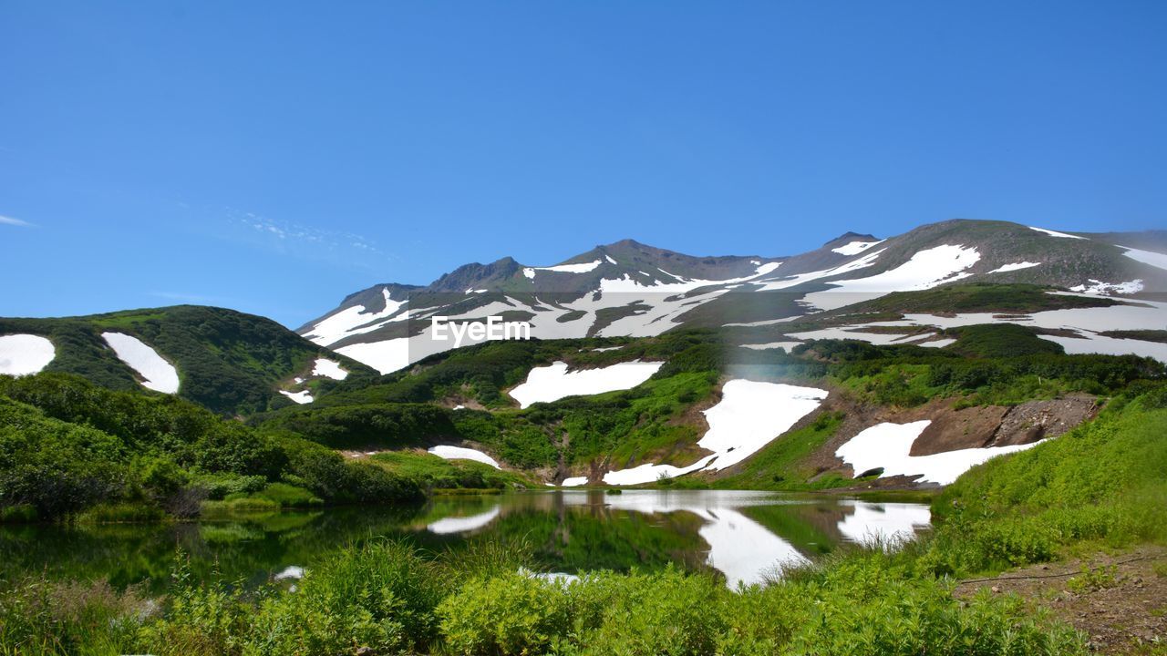 Scenic view of lake and mountains against clear blue sky