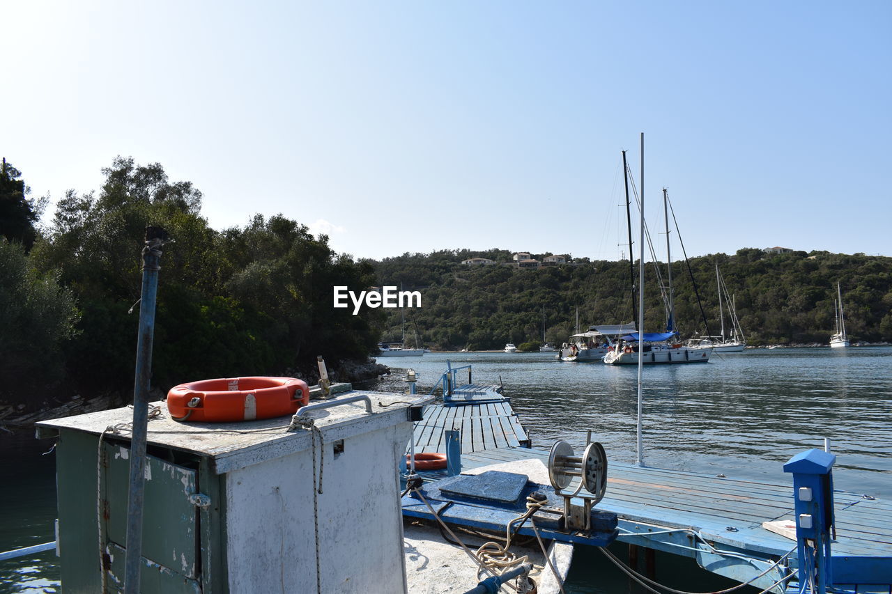 water, nautical vessel, transportation, mode of transportation, boat, sky, nature, dock, vehicle, moored, clear sky, tree, sea, marina, no people, day, boating, watercraft, ship, travel, harbor, tranquility, plant, land, outdoors, pier, blue, beach, travel destinations, sailboat, sunny, scenics - nature, tranquil scene, vacation, holiday, beauty in nature, pole, trip, bay, sunlight, waterway, environment, mast