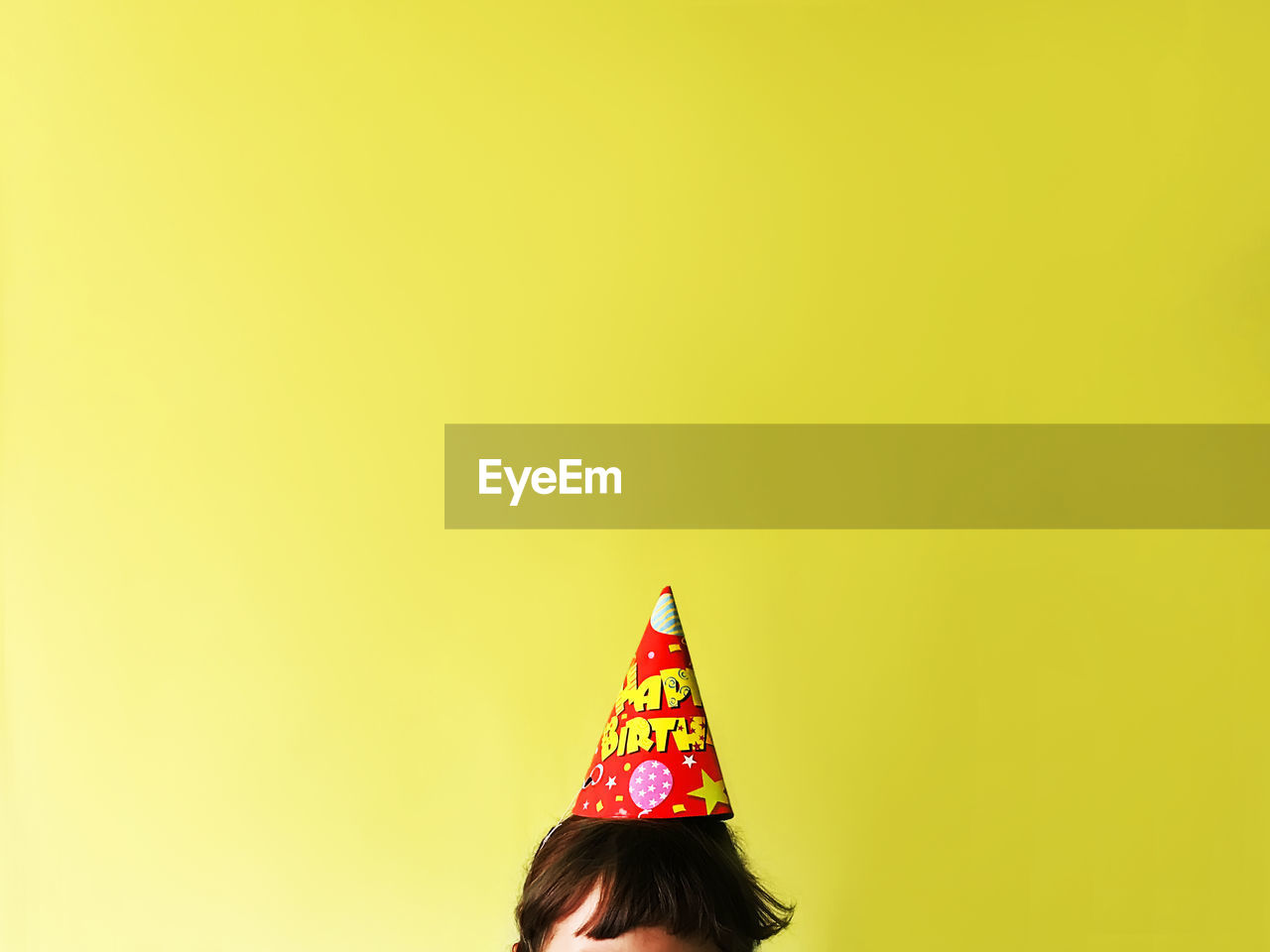 Child wearing party hat against yellow wall