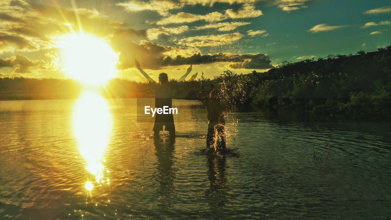 People enjoying in lake against cloudy sky at sunset