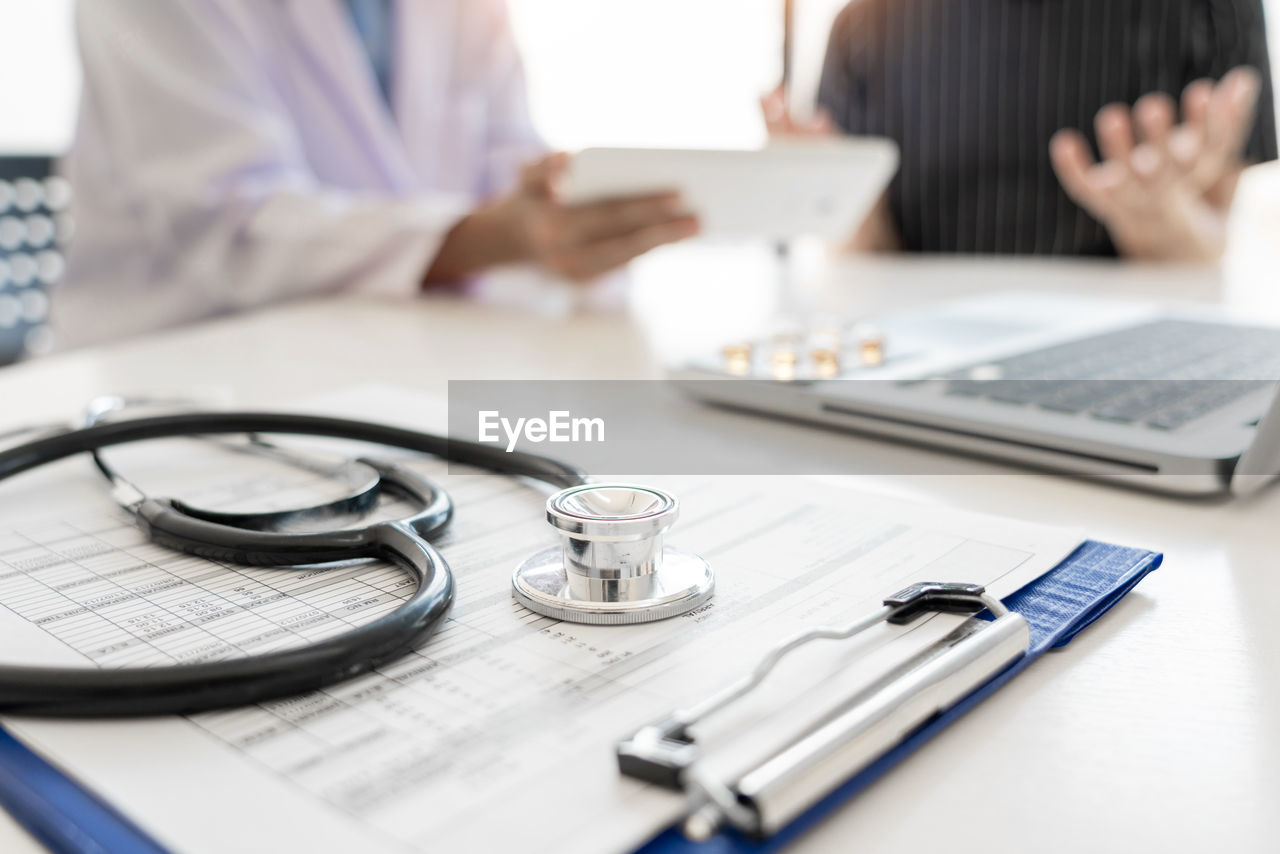 Close-up of stethoscope on clipboard with doctor and patient in background