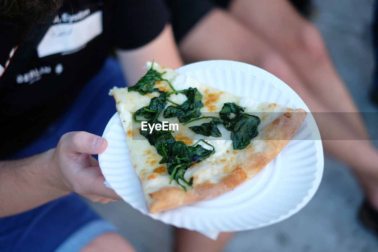Cropped image of person holding pizza in plate while standing outdoors