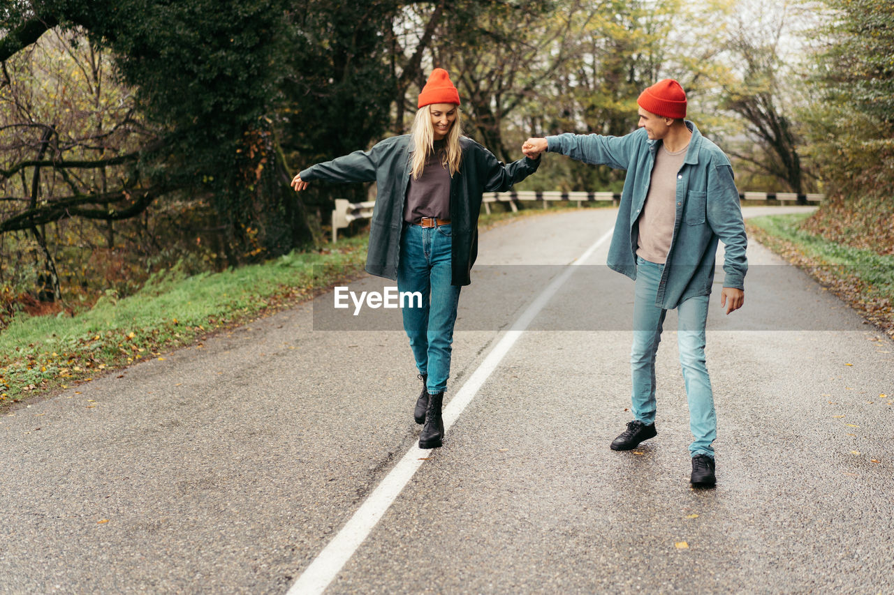 Young cheerful man and woman in love walk along the road holding hands.